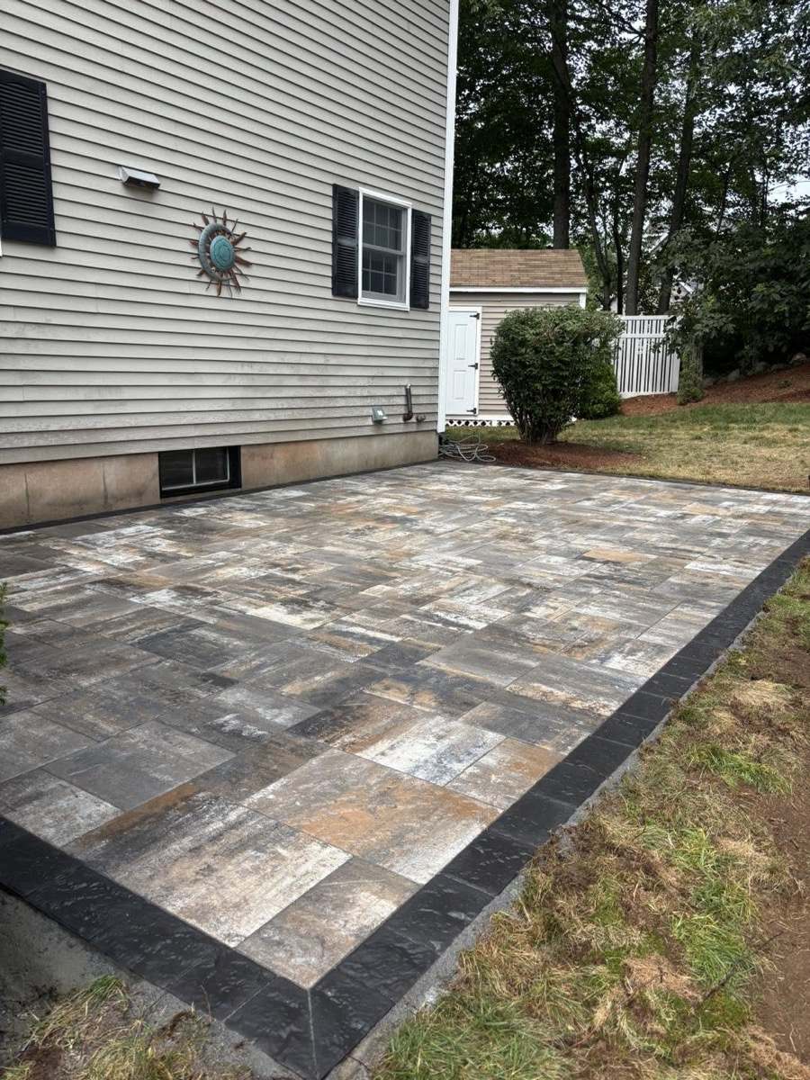 Rustic wood-look paver patio beside a gray house